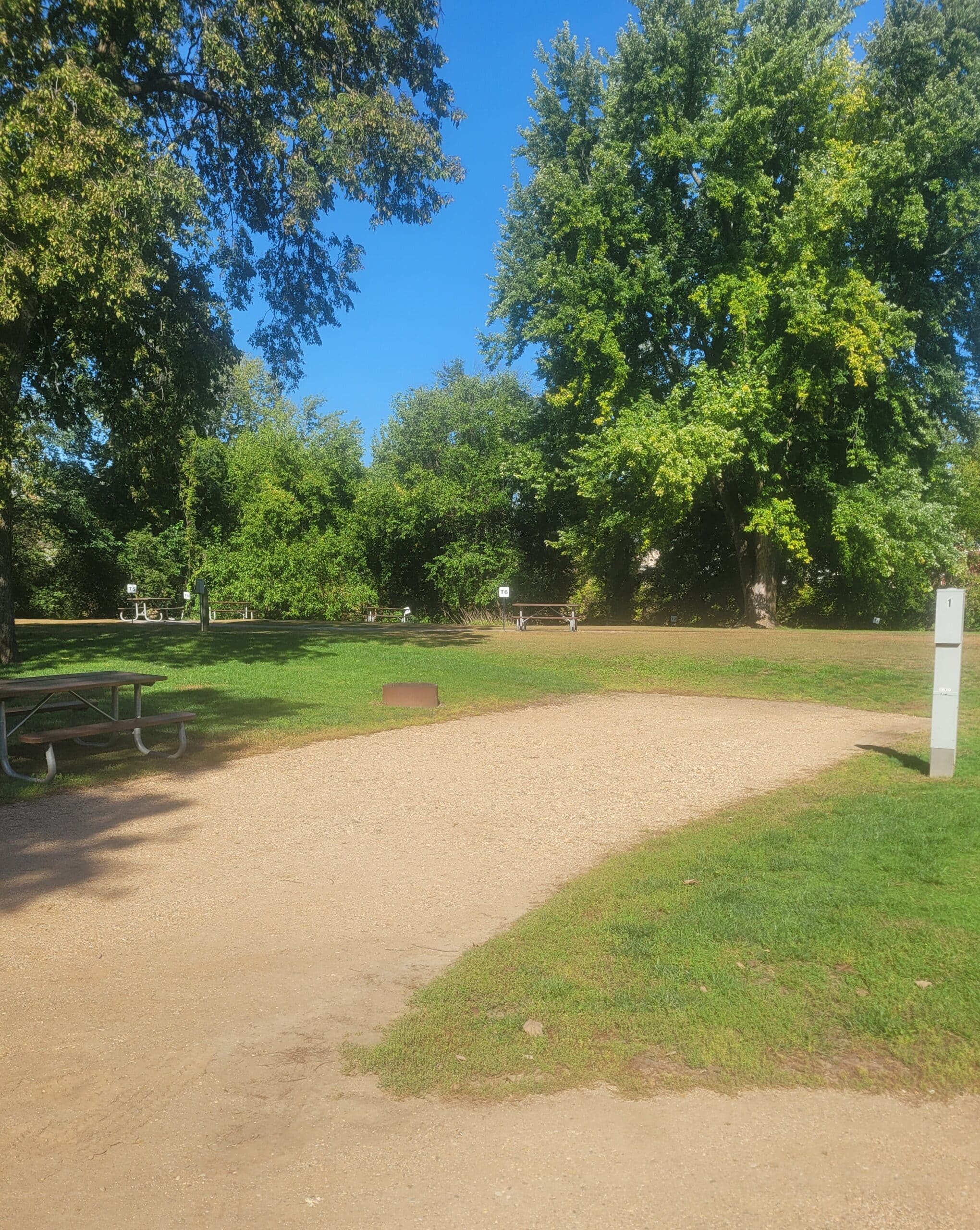 campground site campground site 1 with a gravel path, trees, green grass picnic table and a building