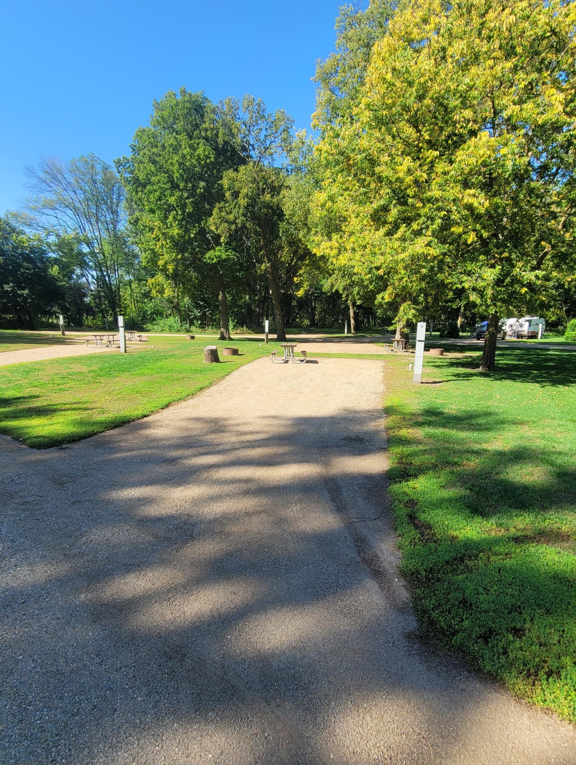 campground site campground site 10 with a gravel path, trees, green grass picnic table and a building