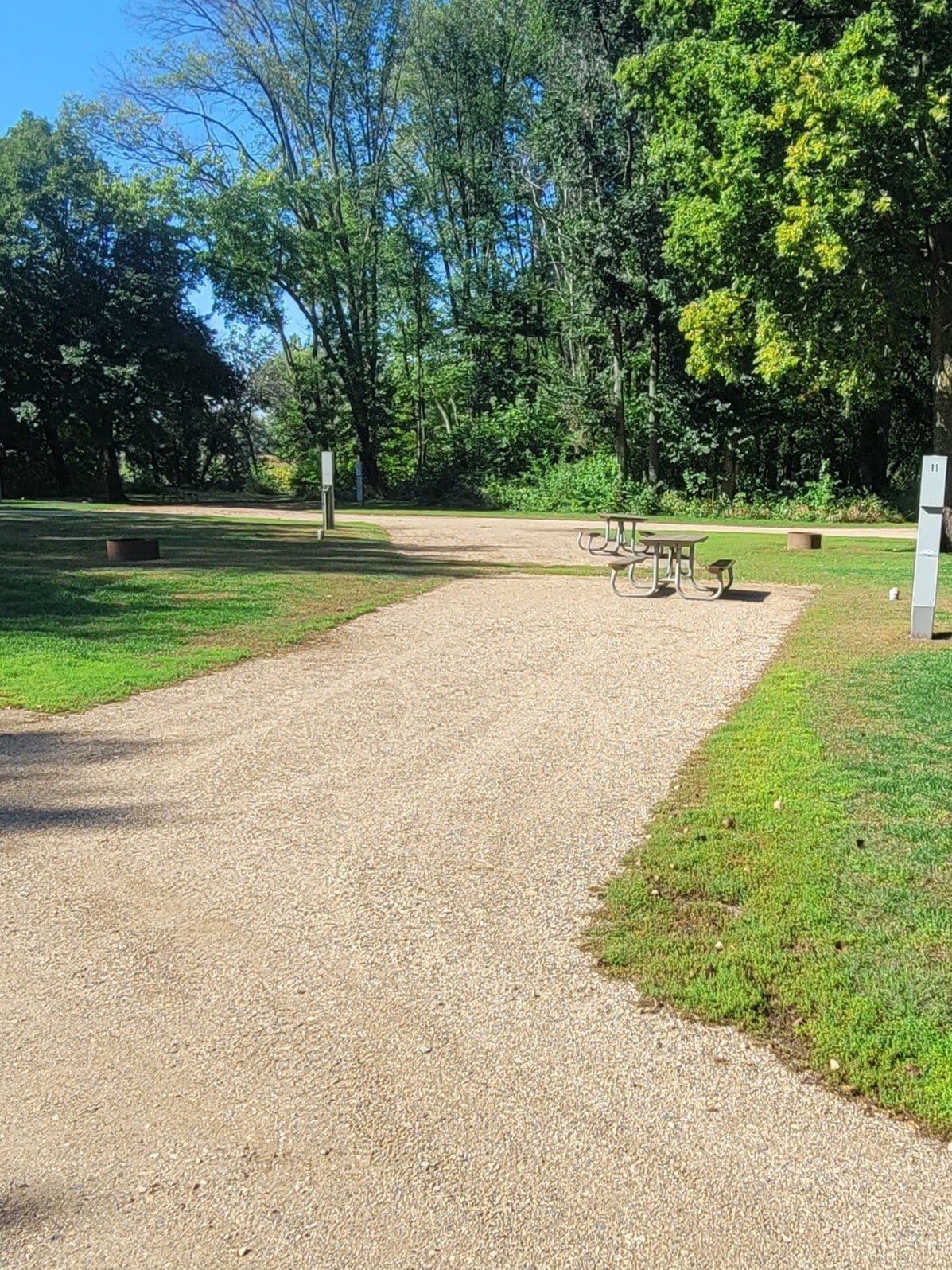 campground site 11 with a gravel path, trees, green grass and picnic tables