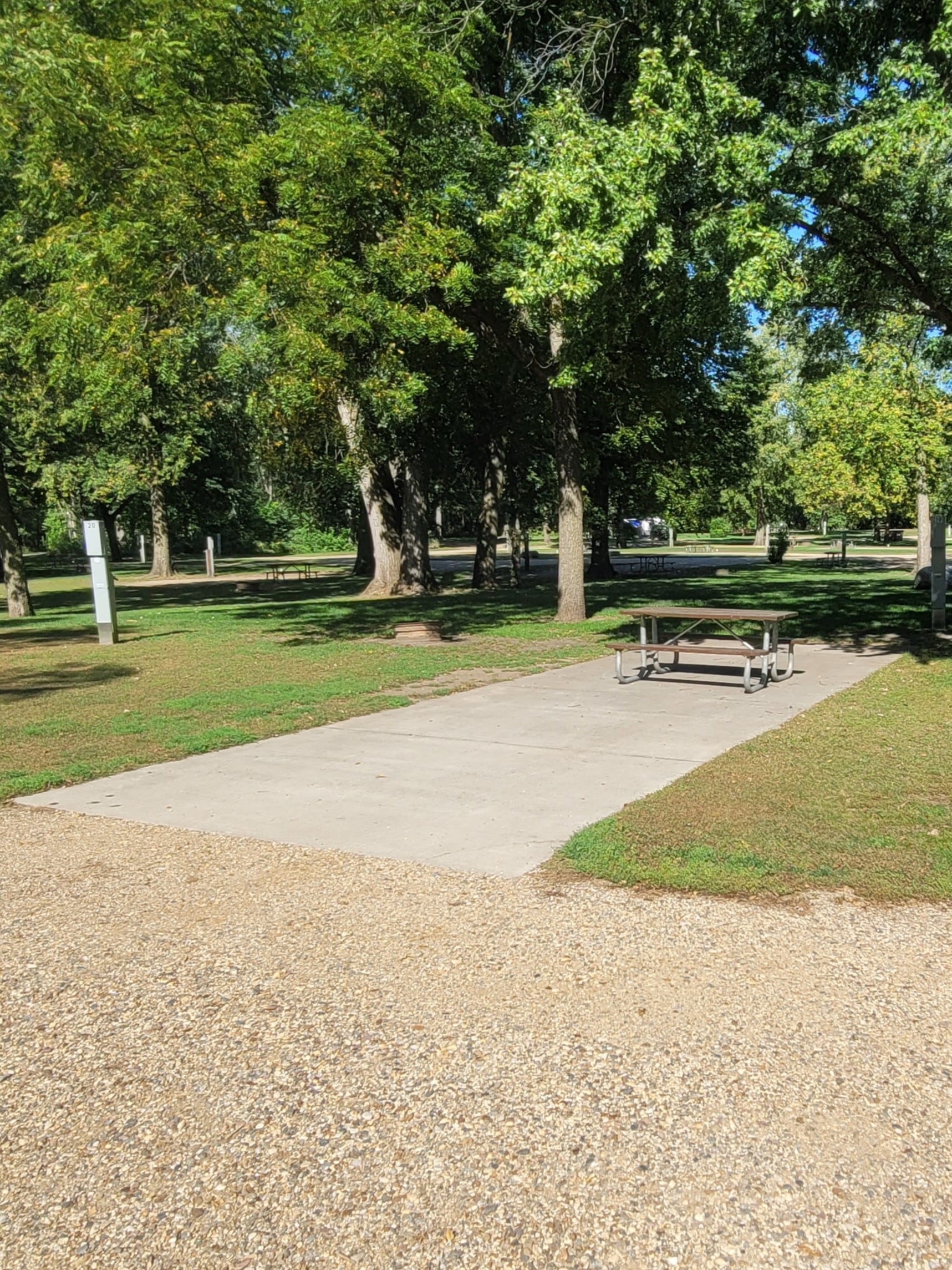 campground site campground site 19 with a wide gravel path, trees, green grass and a picnic table