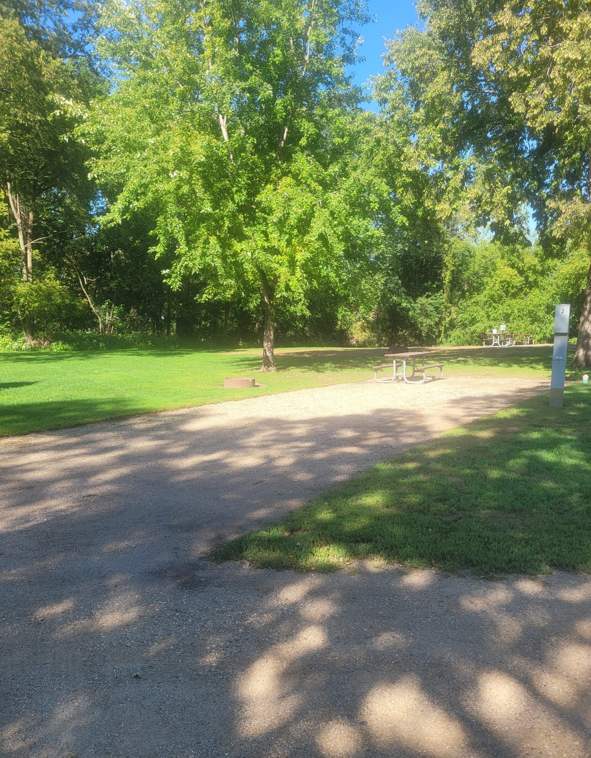 campground site 2 with a gravel path, trees, green grass and a picnic table